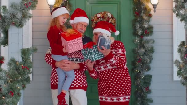 Glückliche Senioren-Großeltern mit Enkelin halten viele Geschenkboxen in der Nähe von Weihnachtshaus, feiern — Stockvideo