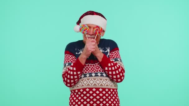 Grandfather in Christmas sweater holding candy striped lollipops hiding behind them fooling around — Stock Video