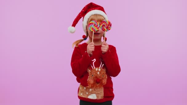 Gadis ceria dengan sweater Tahun Baru memegang permen lolipop bergaris-garis bersembunyi di belakang mereka, bermain-main — Stok Video