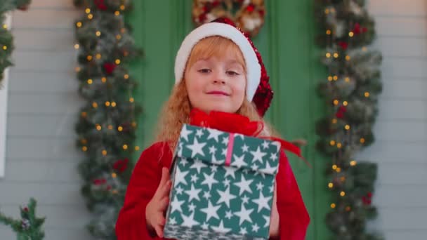 Happy toddler child girl kid in red sweater gifting one Christmas present box, stretches out hands — Stock Video