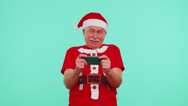 忧心忡忡的祖父穿着圣诞T恤，兴致勃勃地在手机上玩赛车游戏 — 图库视频影像