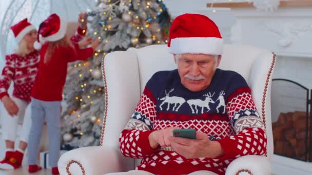 Yaşlı büyükbaba Noel hediyesi alıyor. Evde cep telefonuyla alışveriş yapıyor. — Stok video
