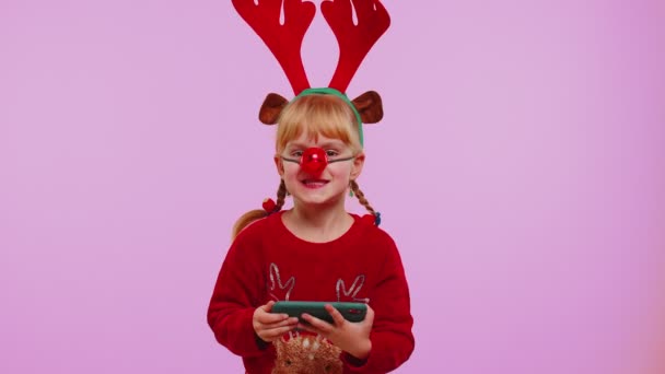 Menina preocupada em chifres de veado de Natal jogando entusiasticamente jogos de corrida no telefone móvel — Vídeo de Stock