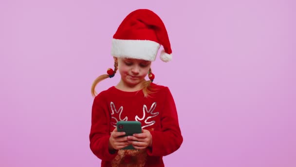 Chica en jersey de Navidad, sombrero usando el teléfono móvil escribiendo nuevo post en la web, compras en línea, navegación — Vídeo de stock
