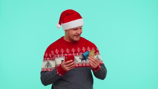 Man in Christmas πουλόβερ χρησιμοποιώντας πιστωτική κάρτα τράπεζα, smartphone κατά τη μεταφορά χρημάτων online ψώνια — Αρχείο Βίντεο