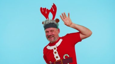 Tişörtlü yetişkin bir adam Noel Baba şapkasıyla dans ederek dans ediyor ve eğleniyor.