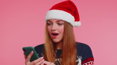 Şık bir Noel kazağı giyen, akıllı telefon görünümlü, neşeli, başarılı bir zafer kazanan kadın.