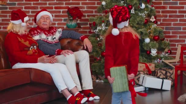 Granddaughter gifting Christmas Xmas present box to amazed happy grandparents at home, celebrating — Stock Video