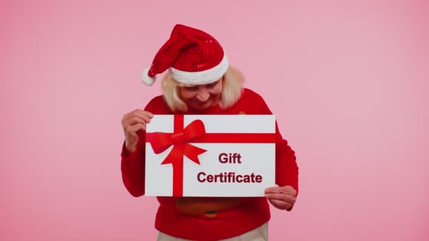 Oudere oma vrouw in nieuwjaar trui presenteren kaart cadeaubon coupon winnaar voucher — Stockvideo