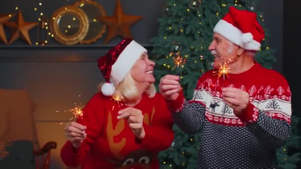 Счастливая взрослая семейная пара в праздничной одежде машет бенгальскими огнями дома, в канун Рождества — стоковое видео