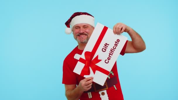 Hombre en camiseta roja Santa sombrero de Navidad presentando tarjeta de regalo vale de cupón de regalo para el ganador — Vídeos de Stock