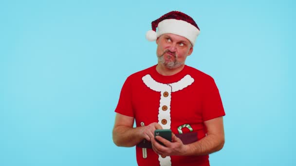 Noel tişörtlü bir adam, cep telefonu kullanan bir şapka internette yeni bir gönderi yazıyor, online alışveriş yapıyor, internette geziniyor. — Stok video