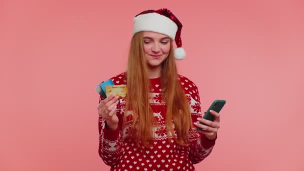 Dívka ve vánočním svetru pomocí kreditní karty, smartphone, převod peněz nakupování on-line — Stock video