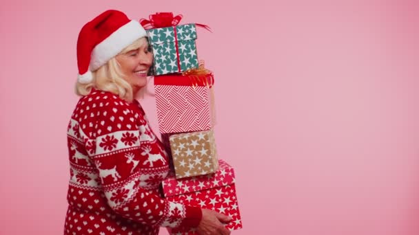 Зріла бабуся в різдвяному светрі тримає багато подарункових коробок продажу новорічних подарунків — стокове відео