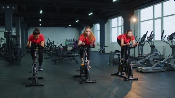 Grupo de chicas realiza entrenamiento aeróbico rutina de ejercicios cardiovasculares en simuladores de bicicleta, entrenamiento en bicicleta — Vídeos de Stock