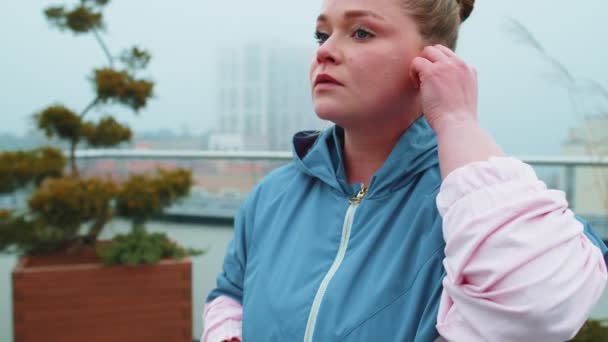 Sport Fitness mujer lleva auriculares inalámbricos en el inicio de su entrenamiento en el techo de la casa — Vídeos de Stock