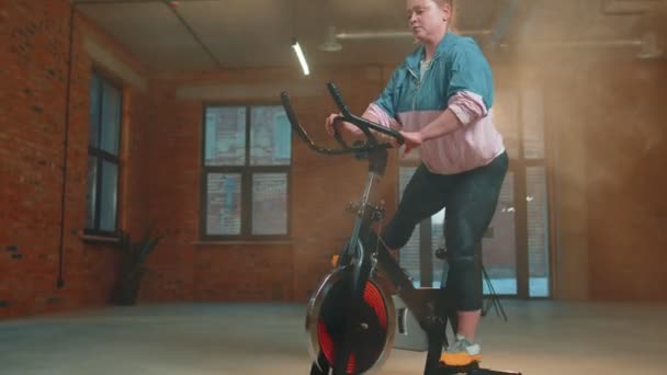 Atletická žena na koni na točení stacionární kolo trénink rutina v oparu tělocvična, hubnutí uvnitř — Stock video
