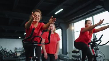 Sağlıklı bir beyaz kadın grubu spor salonunda sabit bisiklet üzerinde egzersiz yapıyor.