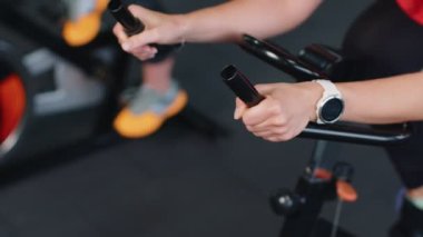 Yakın plan atletik kadın stabil bisiklet bisikleti üzerinde egzersiz yapıyor, kapalı alanda.