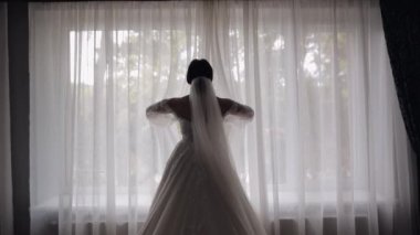 Beyaz elbiseli gelin pencerenin yanında kal ve perdeleri aç, gecelikli ve peçeli kadın.