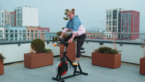 Mulher atlética montando na rotina de treinamento de bicicleta estacionária girando no telhado da casa, perda de peso — Vídeo de Stock