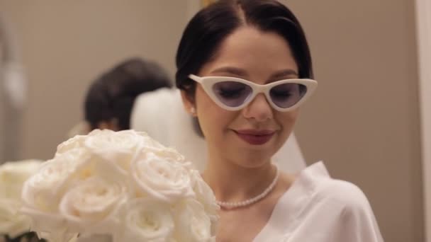 Szekrény gyönyörű elegáns menyasszony lány napszemüvegben nézi a kamerát és mosolyog, esküvő reggel — Stock videók