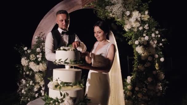 Newlyweds cut the wedding cake, lovely bride and groom couple cutting dessert with a knife outdoors — 图库视频影像