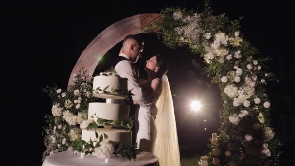 Newlyweds making a kiss near cake, lovely bride and groom couple with three-tiered wedding dessert — 图库视频影像