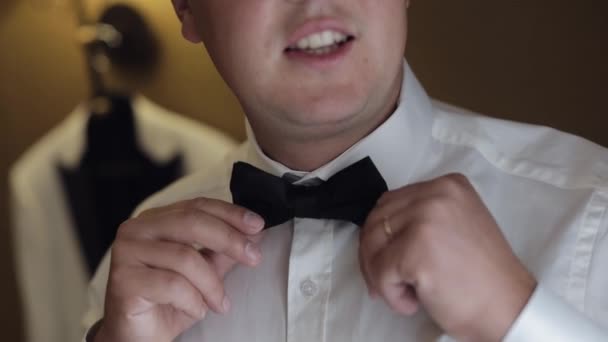 Жених настраивает галстук-бабочку, готовится идти к невесте, бизнесмен в белой рубашке, день свадьбы — стоковое видео