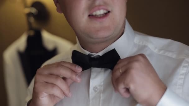 Groom man adjusts bow tie, preparing to go to the bride, businessman in white shirt, wedding day — Stock Video