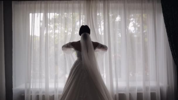 Sposa in abito boudoir bianco soggiorno vicino alla finestra e l'apertura di tende, donna in abito da notte e velo — Video Stock