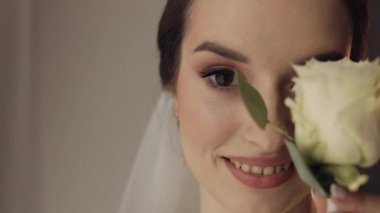 Gelin kızın güzel yüzüne yakın çekim. Kameraya bakıyor ve çiçek buketiyle gülümsüyor.