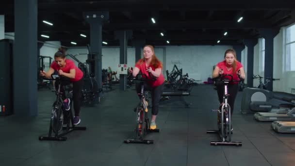 Gezonde Kaukasische groep vrouwen die trainen op een stationaire fiets in de fitnessruimte — Stockvideo