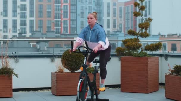 건강 한 백인 여성, 집 옥상 체육관에서 고정 자전거타기 운동을 하는 모습 — 비디오