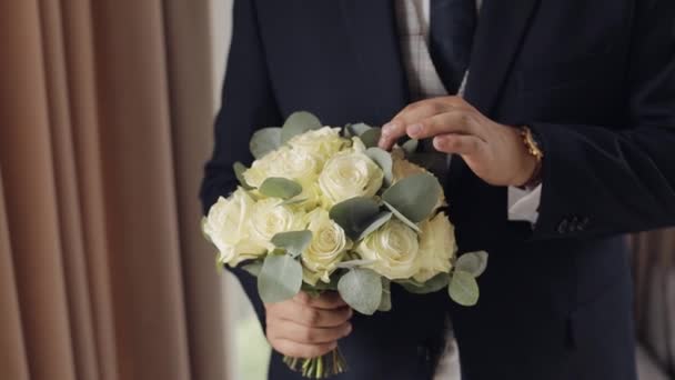 Жених со свадебным букетом в руках дома готовится к выходу невесты, крупным планом замедленной съемки — стоковое видео