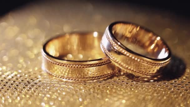 Свадебные кольца лежали, вращались, вращались на блестящей золотистой сияющей поверхности с легким крупным планом — стоковое видео