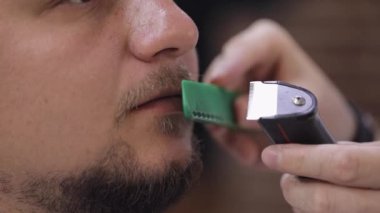 Berber sakal keserken elektrikli makina kullanır, berber dükkanında seyis müşterisine saç tıraşı yapar.