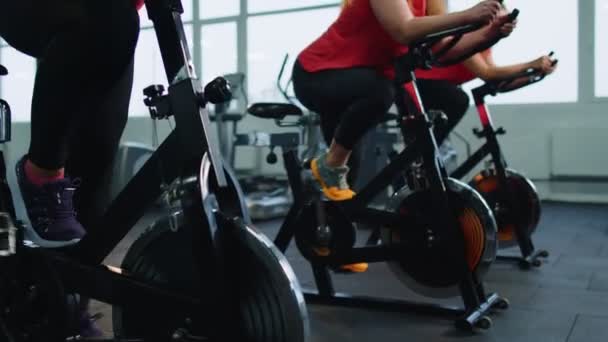 Group athletic girls performing aerobic riding training exercises on cycling stationary bike in gym — Vídeo de Stock