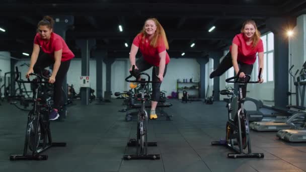 Athletic women group riding on spinning stationary bike training routine in gym, weight loss indoors — Stock Video