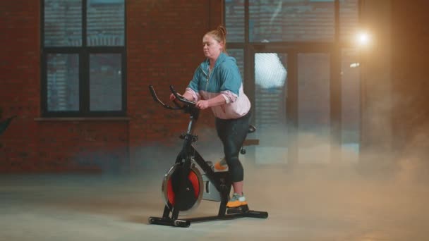 在雾蒙蒙的健身房进行自行车自行车有氧骑行训练的女运动员 — 图库视频影像
