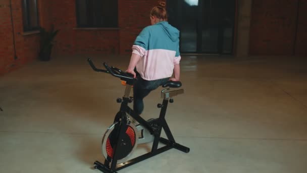 Atletisch meisje maken acrobatische truc op fiets oefening workout op stationaire fiets machine binnen — Stockvideo