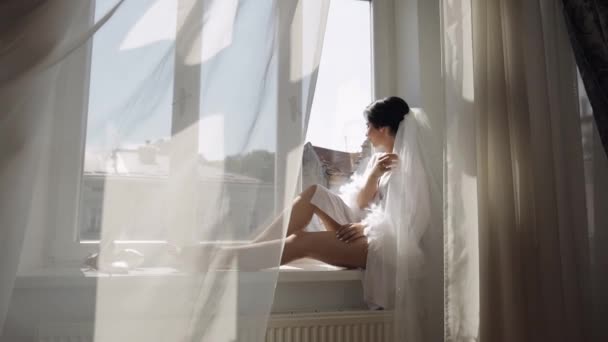 Brud i boudoir klänning sitter på fönstret tröskel bröllop morgon förberedelser kvinna i nattlinne, slöja — Stockvideo