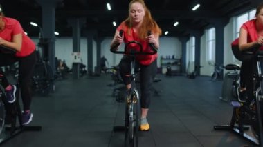 Spor salonunda bisiklet çevirme antrenmanına katılan atletik kadın grubu, içeride kilo kaybı.
