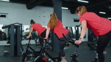 Sağlıklı bir beyaz kadın grubu spor salonunda sabit bisiklet üzerinde egzersiz yapıyor.