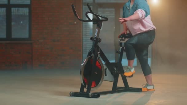 Sportliche Frau reitet auf Spinning stationärem Fahrrad Trainingsprogramm in Dunst Turnhalle, Gewichtsverlust in Innenräumen — Stockvideo