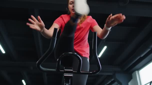 Αθλητικό κορίτσι εκτελεί άλματα αερόβια ιππασία ασκήσεις κατάρτισης για ποδήλατο στατικό ποδήλατο στο γυμναστήριο — Αρχείο Βίντεο