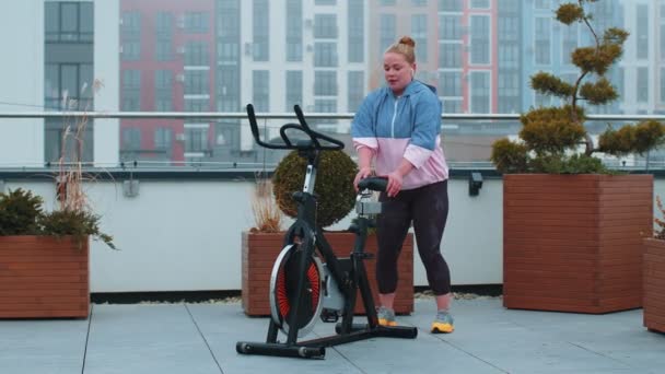 Mulher caucasiana saudável exercitando treino na bicicleta estacionária da máquina de ciclismo no ginásio da cobertura da casa — Vídeo de Stock