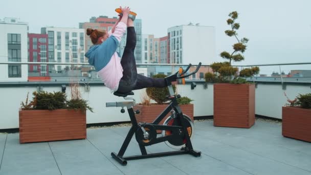 陸上競技の女性は、屋根の上で静止自転車を回転させる上で双子の訓練ルーチンを作ります,減量 — ストック動画