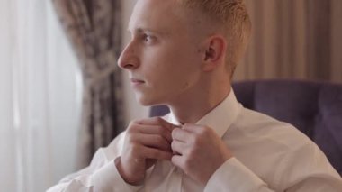 Ceketli şık adam düğmelerini ilikliyor, beyaz gömleğini ilikliyor ve pencerenin yanına gitmeye hazırlanıyor.