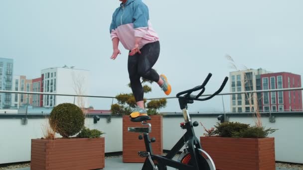 運動女性は、静止自転車を回転させる上でアクロバティックなトレーニングトリックワークアウトを飲み込む — ストック動画